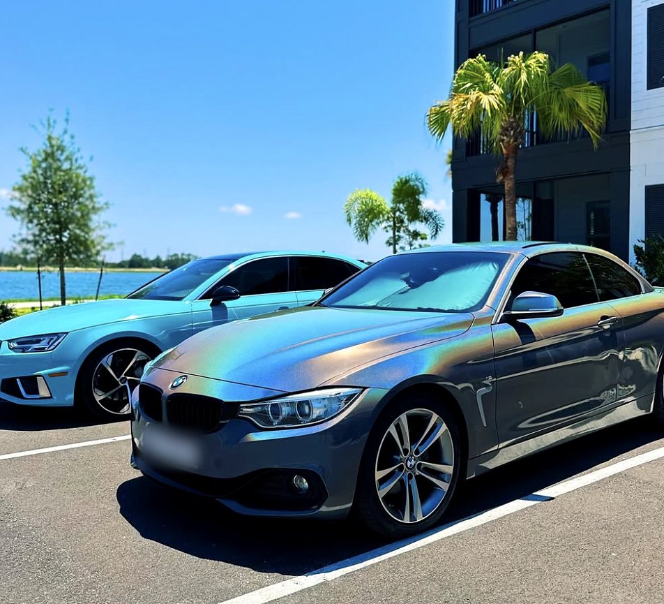 BMW 4 Series convertible in a color-shifting gray wrap, parked beside the blue Audi